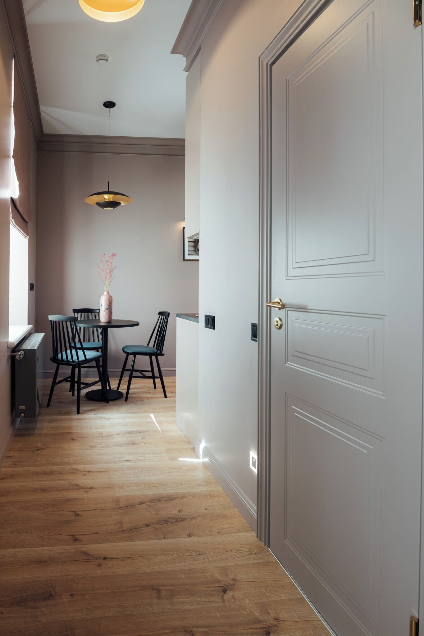 A hallway with a wooden floor, a white door, and a dining area with a table and chairs.