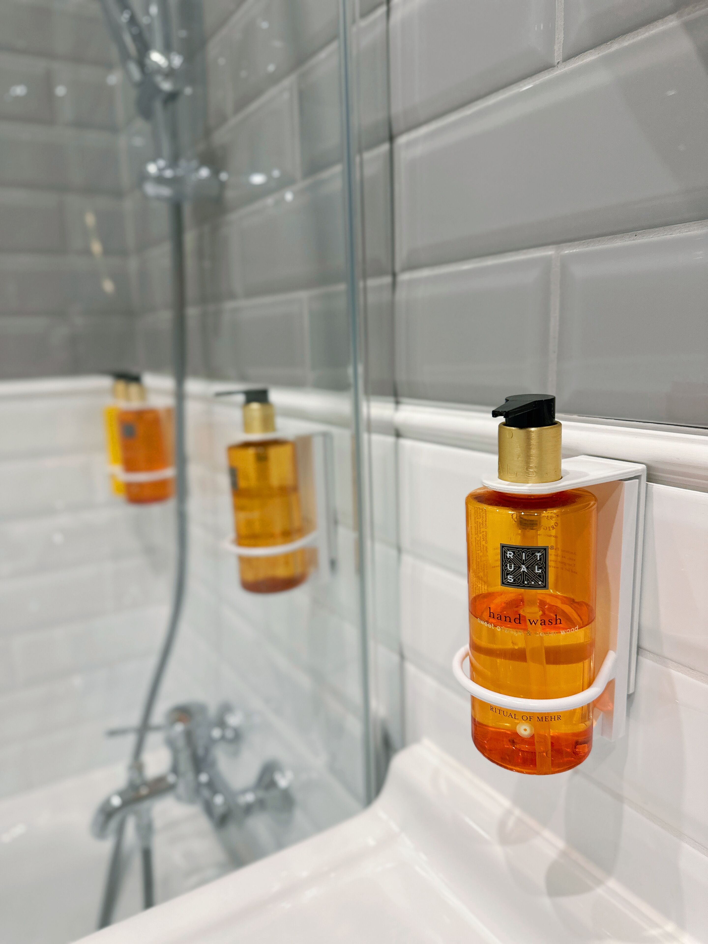 A bathroom with a glass shower enclosure, a white bathtub, and two bottles of handwash on a white towel rack.
