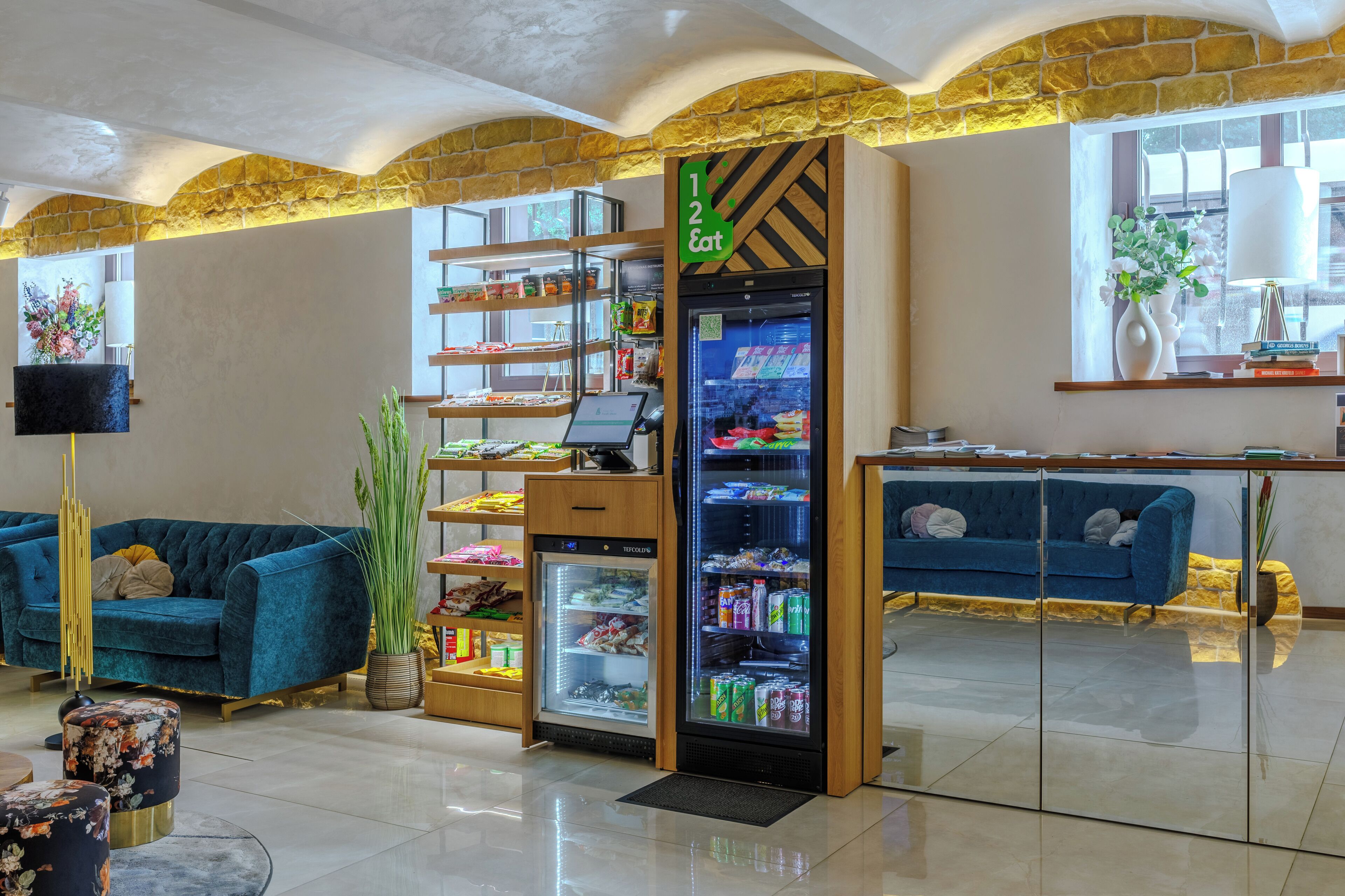 A lobby with a blue sofa, a refrigerator with snacks, and a TV on the wall.