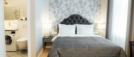 Ein Schlafzimmer mit einem großen Bett, einem Nachttisch, einer Wandleuchte und Blick auf ein Badezimmer mit Waschmaschine und Toilette.
