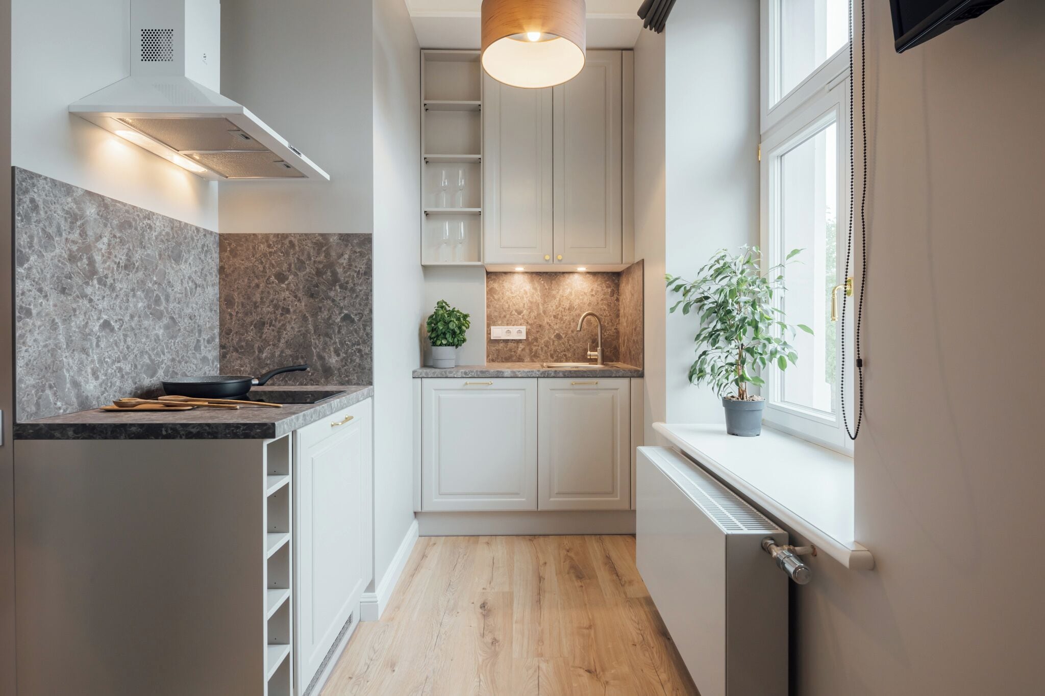 A modern kitchen with white cabinets, a granite countertop, a built-in stove, and a window with a plant on the sill.