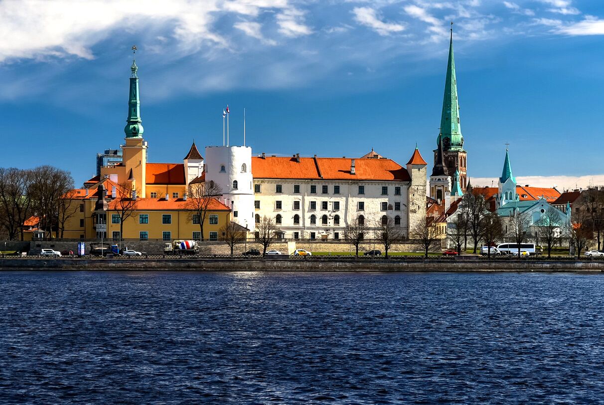 A historic building with multiple spires, a river in the foreground, and a clear sky.
