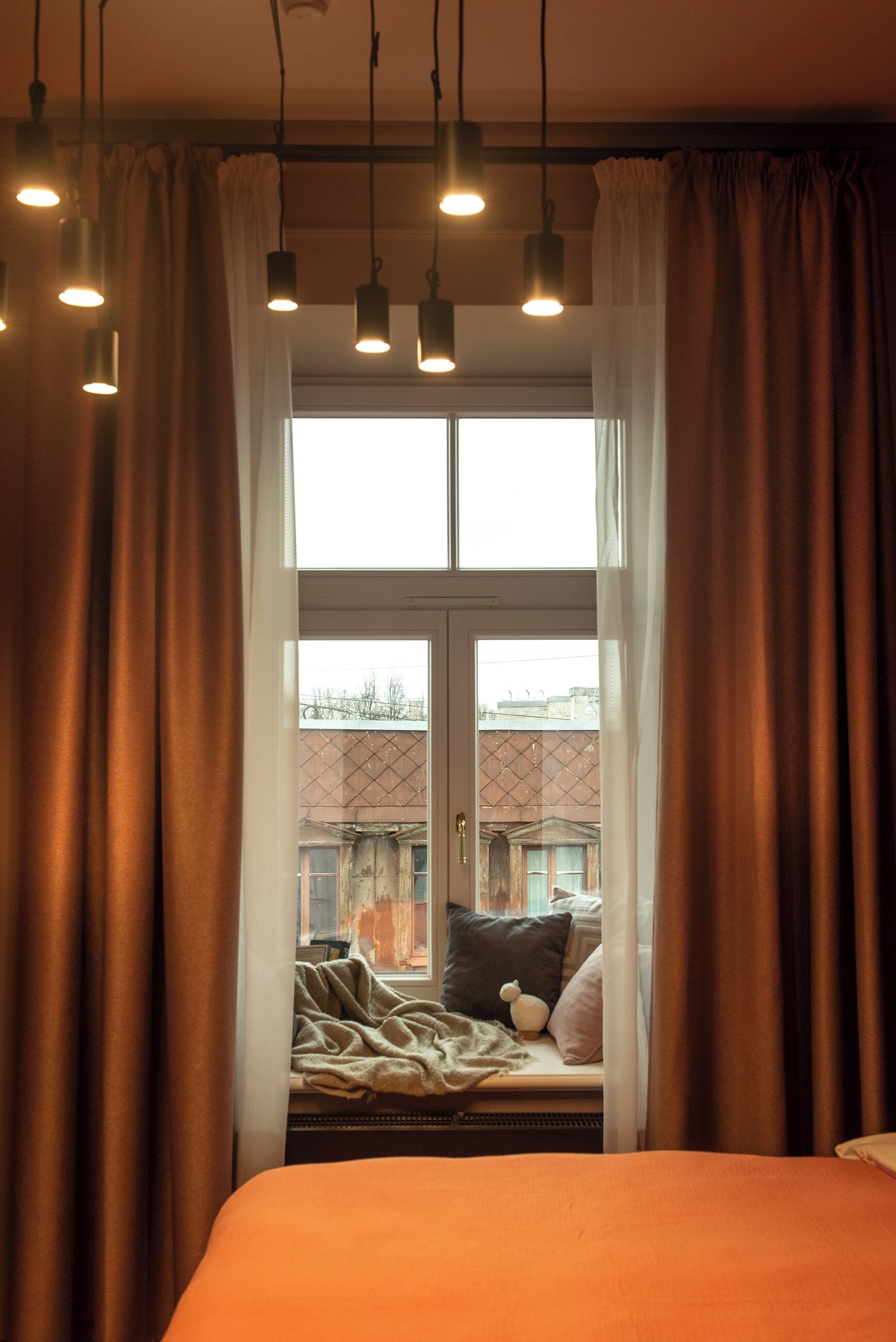 A bedroom with a bed, a window with curtains, and hanging lights.