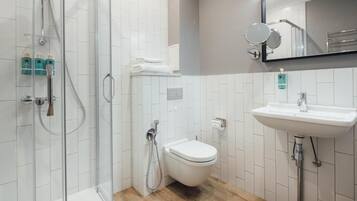 Un baño moderno con cabina de ducha de vidrio, inodoro blanco y lavabo con espejo arriba.