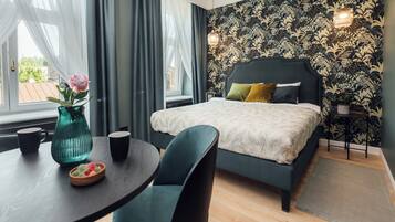 A bedroom with a bed, a table with a vase and cups, and a view of the outside.