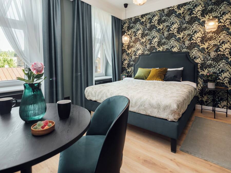 A bedroom with a bed, a table with a vase and cups, and a view of the outside.