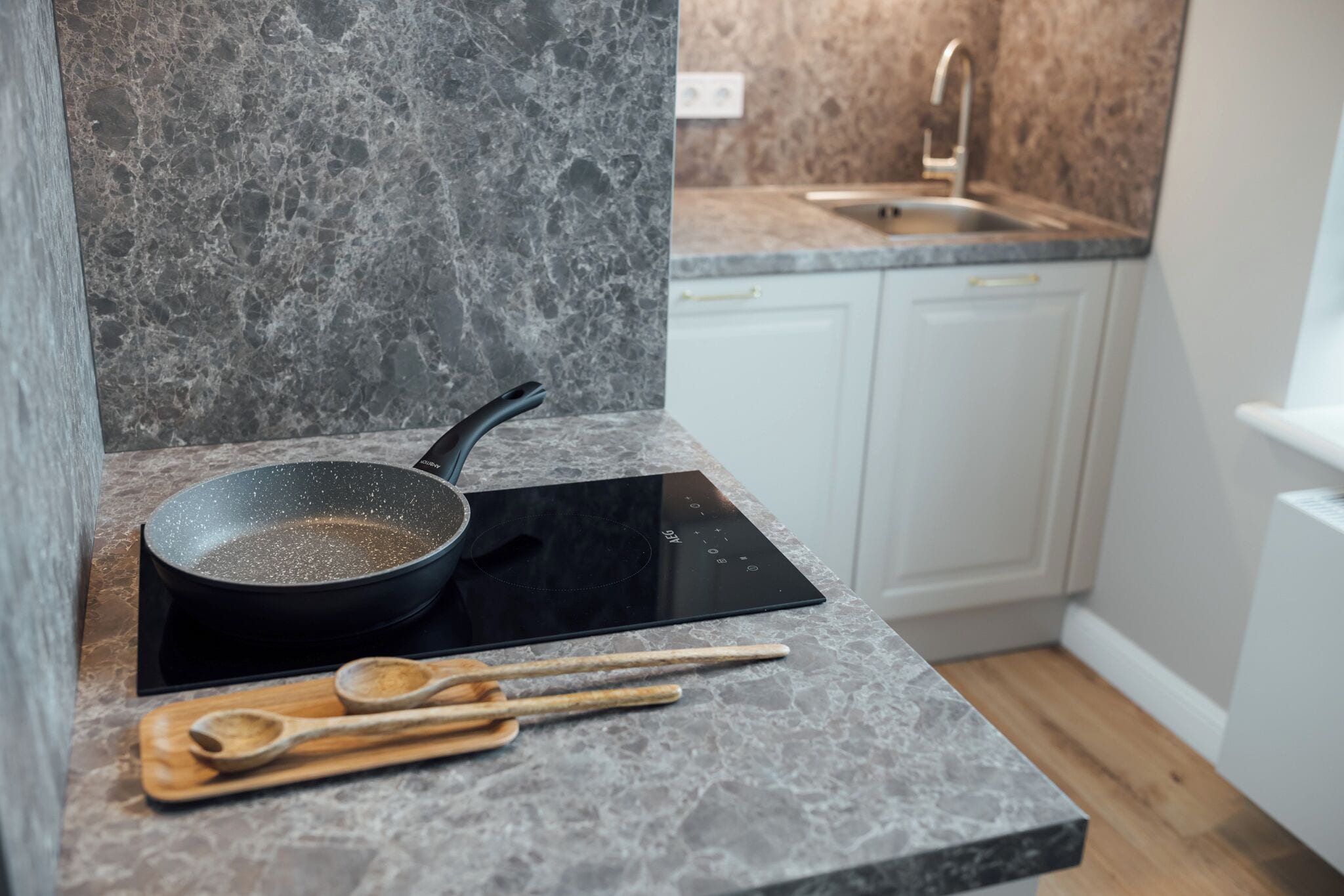 Una cocina con encimera de granito, placa de inducción negra y utensilios de madera sobre una tabla de cortar.