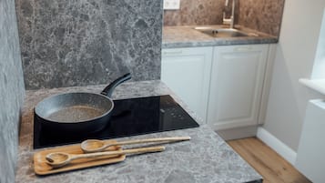 Una cocina con encimera de granito, placa de inducción negra y utensilios de madera sobre una tabla de cortar.