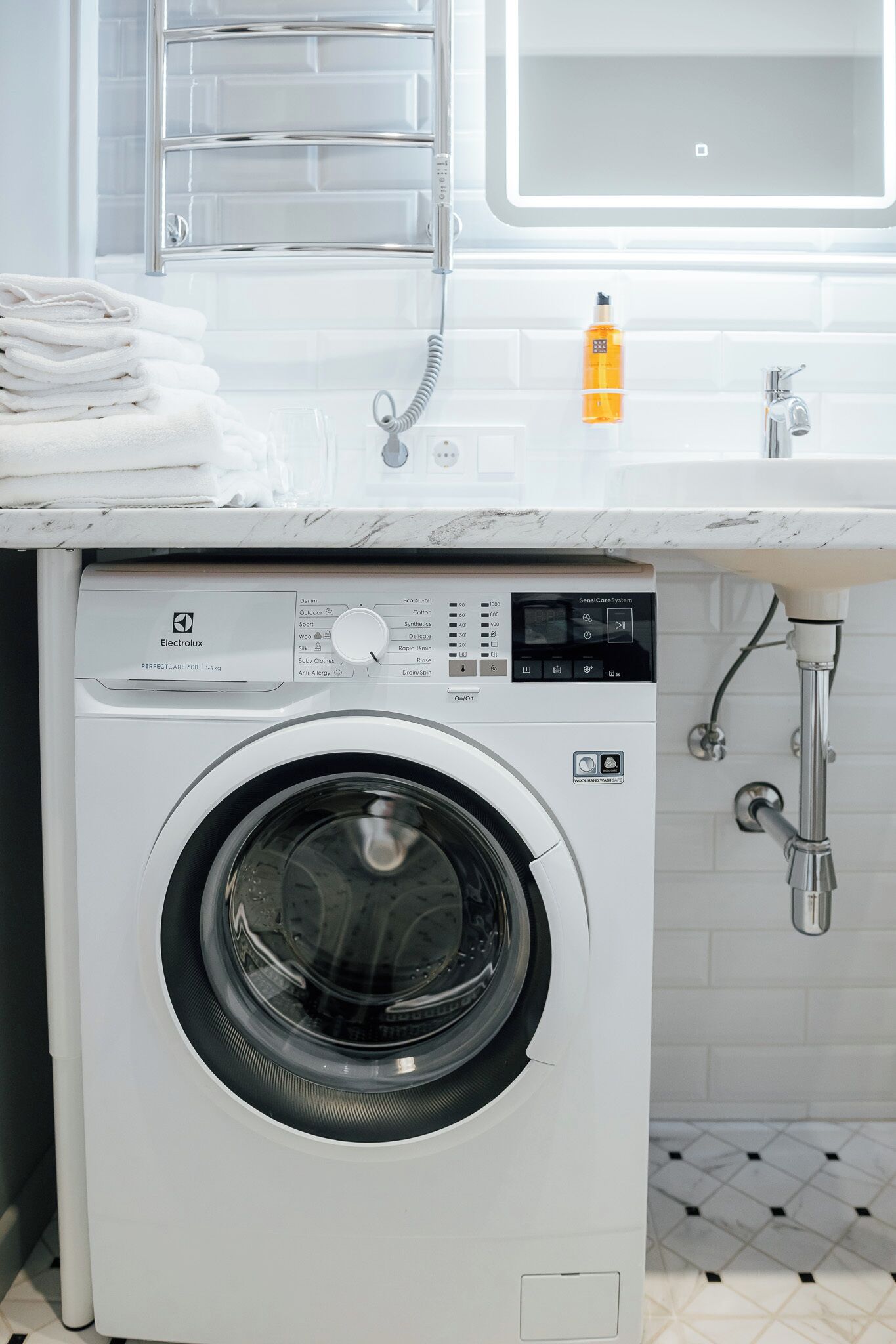 A front-loading washing machine with a control panel, a sink, and a towel rack above it.