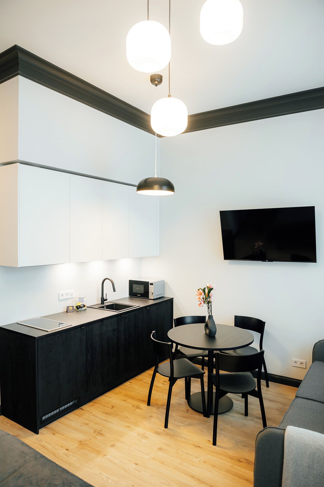 A modern kitchen with a black island, a dining area with a round table and chairs, and a flat-screen TV mounted on the wall.