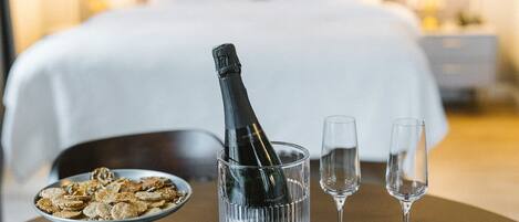 A hotel room with a bed, bedside lamps, a bottle of champagne, two glasses, and a plate of cereal on a table.