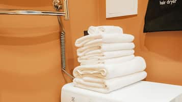 A front-loading washing machine with a control panel, stacked towels, and a hair dryer on the wall.