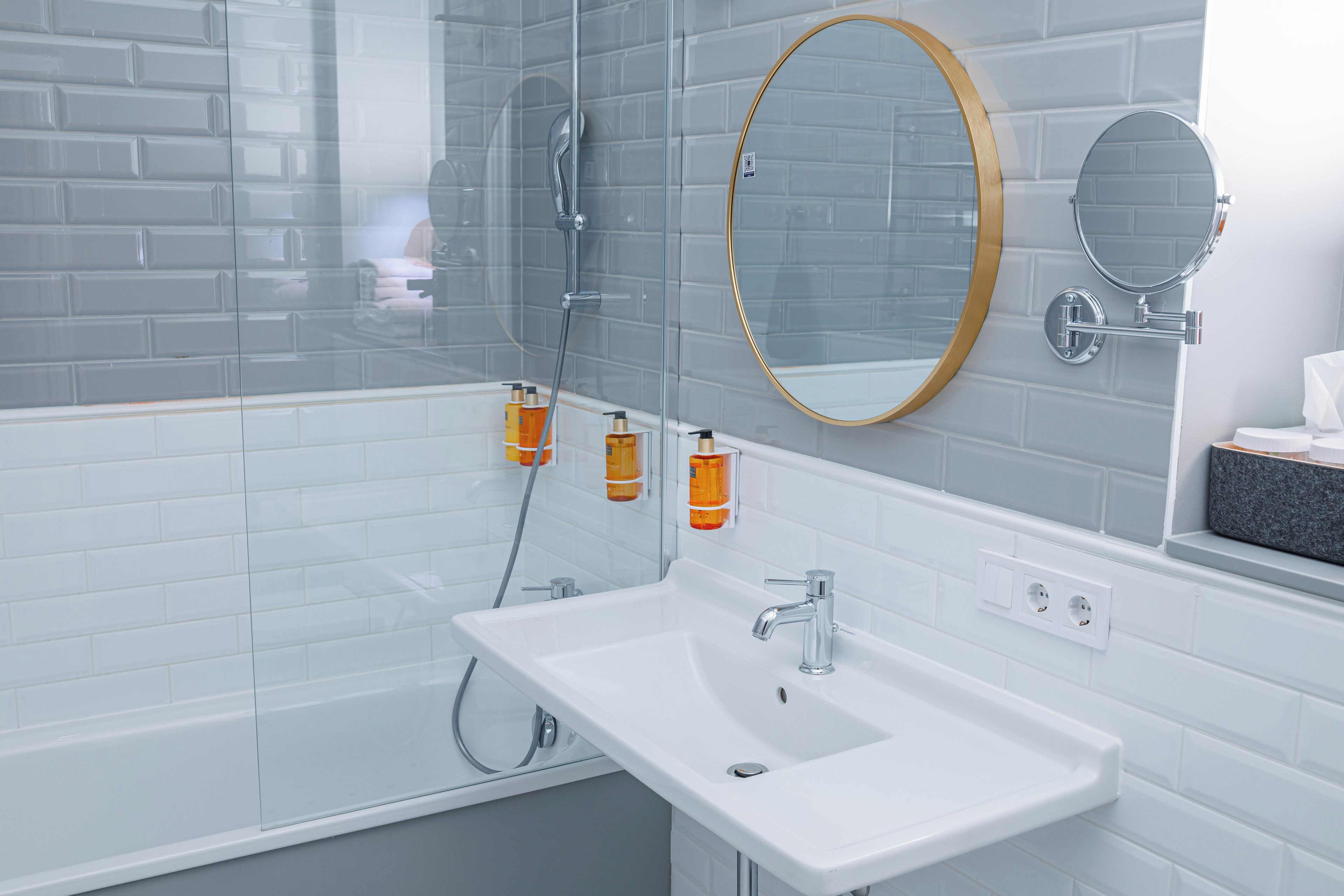 A modern bathroom with a white sink, two mirrors, and a glass shower enclosure.