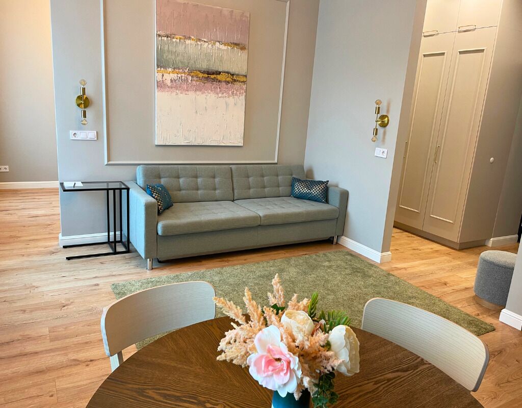 Un salón con un sofá gris, una mesa de centro con un arreglo floral y un cuadro en la pared.