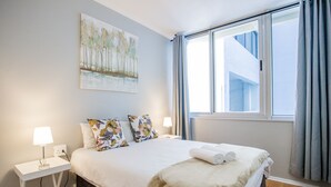 Een slaapkamer met een bed, twee nachtkastjes, een schilderij en een raam met gordijnen.
