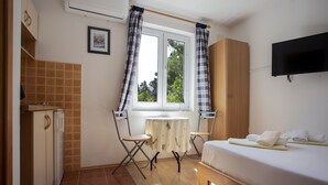 A compact hotel room with a bed, a small table, a chair, a TV mounted on the wall, and a window with curtains.