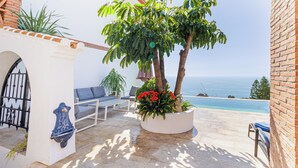 A patio with a pool, a white wall with a decorative blue basin, and a seating area with a view of the sea.