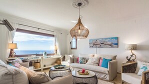 A modern living room with a sofa, coffee table, and a view of the sea.