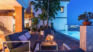 A rooftop terrace with a pool, outdoor seating, and a view of the city at dusk.