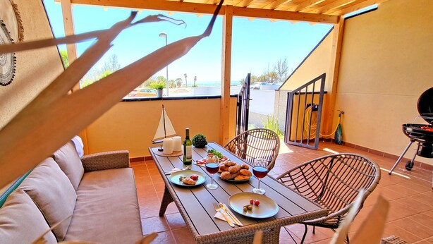 Un patio con una mesa lista para una comida, mobiliario de mimbre y una parrilla.