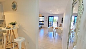 Una cocina moderna con armarios blancos, un área de comedor con mesa y sillas, y vistas al exterior a través de amplios ventanales.