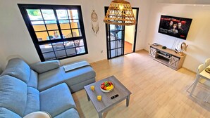 Una sala de estar moderna con un sofá, una mesa de centro con fruta, un televisor y un comedor con desayuno.