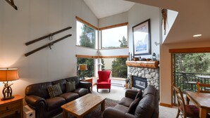 A spacious living room with a fireplace, leather sofas, a red armchair, and large windows offering a view of the outdoors.