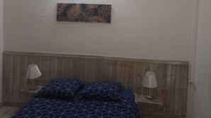 Een slaapkamer met een houten hoofdbord, een bed met een deken met een geometrisch patroon, twee bedlampen en een wandlamp.