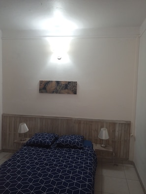 Ein Schlafzimmer mit einem Holz-Kopfteil, einem Bett mit gesteppter Bettdecke mit geometrischem Muster, zwei Nachttischlampen und einer Wandleuchte.