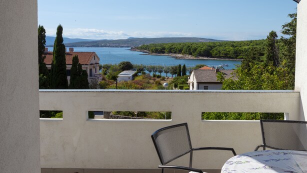 Una terraza con una mesa y sillas, con vista a un lago y edificios y árboles al fondo.