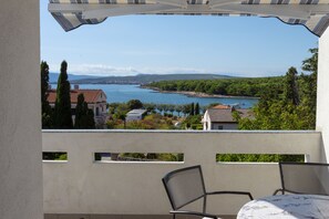 Eine Terrasse mit Tisch und Stühlen, mit Blick auf einen See, im Hintergrund Gebäude und Bäume.
