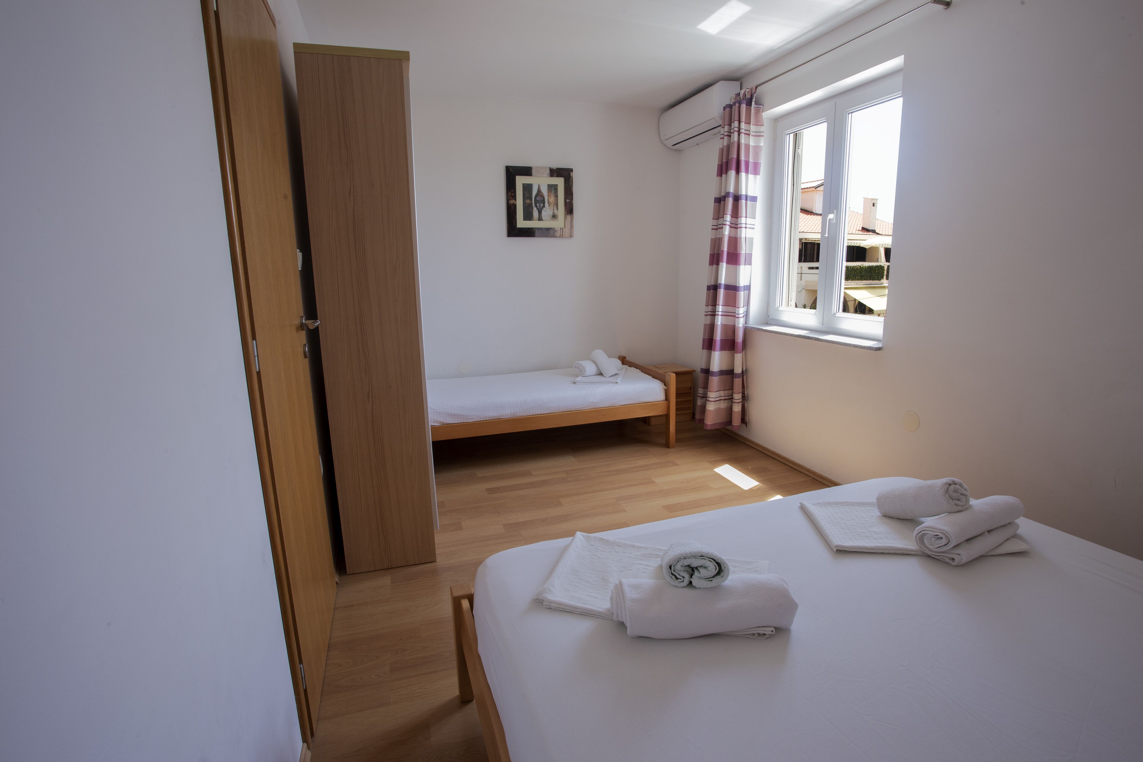 A bedroom with a wooden bed, a smaller bed in the corner, a window with curtains, and a door.