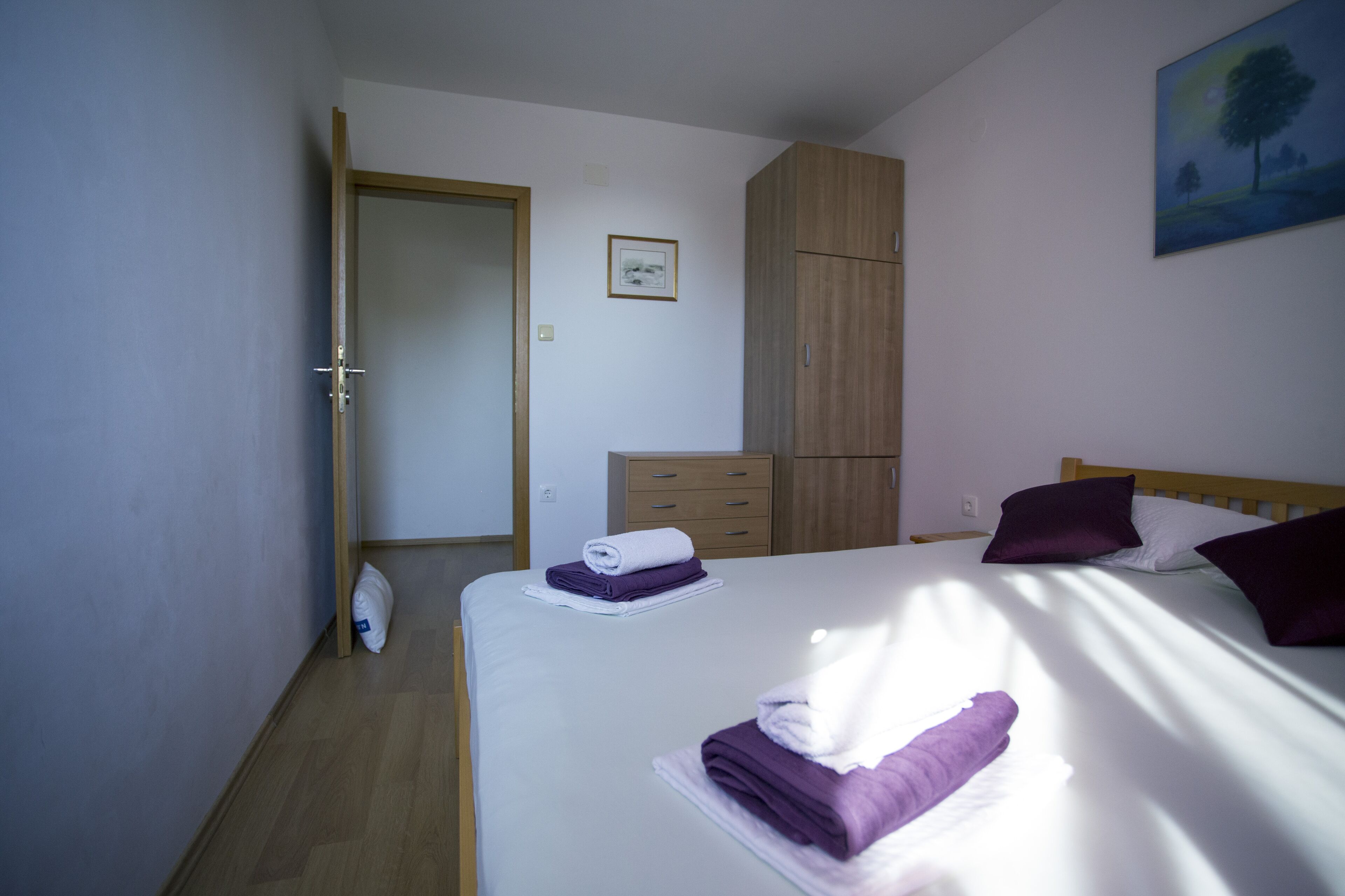 Habitación de hotel con cama, armario, puerta y un cuadro en la pared.
