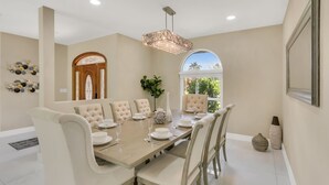 A dining room with a large wooden table, white upholstered chairs, and a chandelier. - Plantation Point: Family Friendly Neighborhood (Plantation)