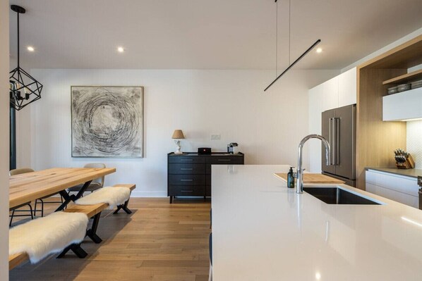 A modern kitchen with a central island, a dining area with benches, and a black cabinet.