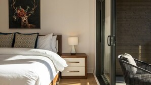 Ein Schlafzimmer mit Bett, Nachttisch, Lampe und Glastür, die auf einen Balkon führt.