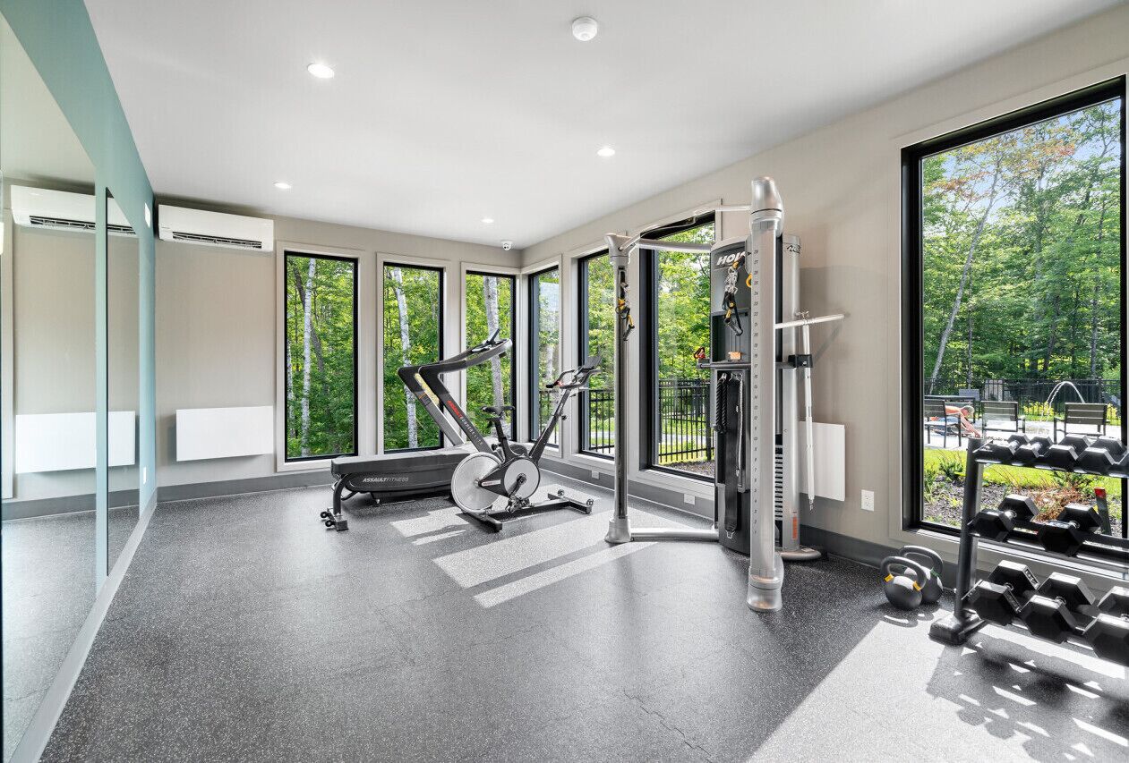 A modern gym with exercise equipment, large windows, and a view of trees.