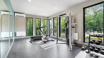 A modern gym with exercise equipment, large windows, and a view of trees.