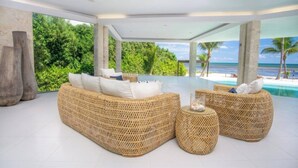 A modern lounge with wicker furniture, a glass coffee table, and a view of the ocean.