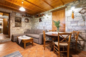 A cozy living room with a stone wall, wooden ceiling, and a dining area with a round table and chairs.