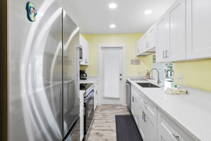 A compact kitchen with white cabinets, a stainless steel refrigerator, a microwave, and a sink.