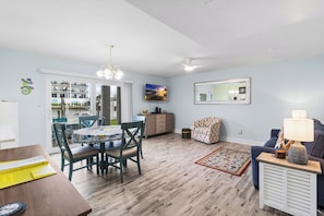 A living room with a sofa, a coffee table, a TV, and a dining area with a table and chairs.