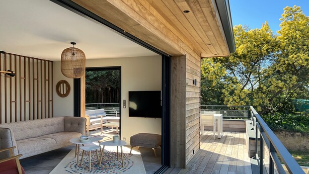 A modern living room with a sofa, coffee table, and TV, connected to an outdoor deck with a railing.
