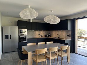 Une cuisine moderne avec des meubles de couleur sombre, des appareils en acier inoxydable, un grand îlot central doté de sièges et une grande fenêtre.