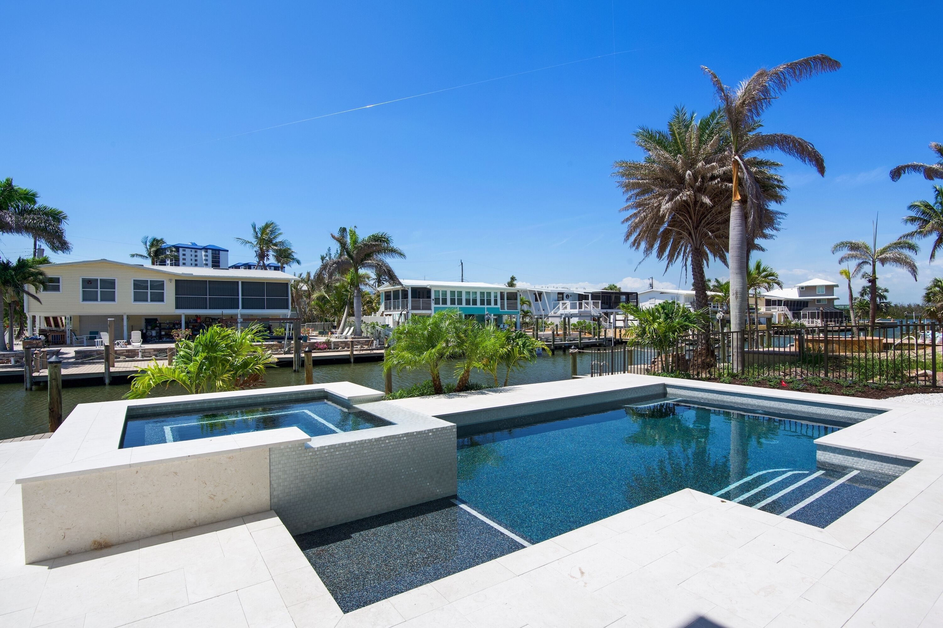 A modern pool area with clear blue water, surrounded by palm trees and a view of a marina with boats.