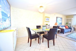 A dining area with a glass table and chairs, a sofa, and a lamp. - Fountainhead 209 1 Bedroom Condo by RedAwning (Ocean City)