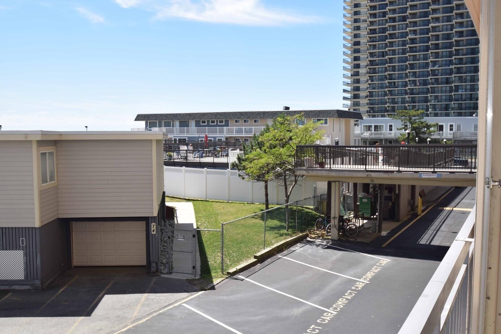 Un parking avec des places délimitées, un pont piétonnier et un bâtiment avec un garage en premier plan.