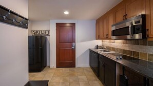 Cocina compacta con armarios de madera, un microondas de acero inoxidable y un refrigerador negro.