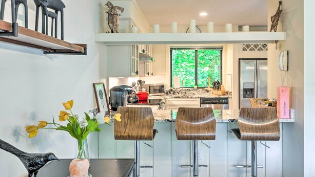 Cozinha moderna com ilha central, banquetas e mesa de jantar com um vaso de flores.