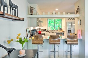 A modern kitchen with a central island, bar stools, and a dining table with a vase of flowers.